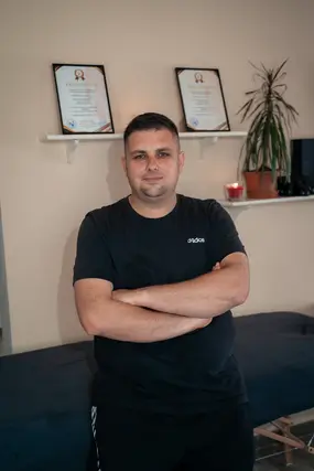 Lacko egy polc elött áll, amin egy sportmasszőri és egy svédmasszőri certifikáció van
